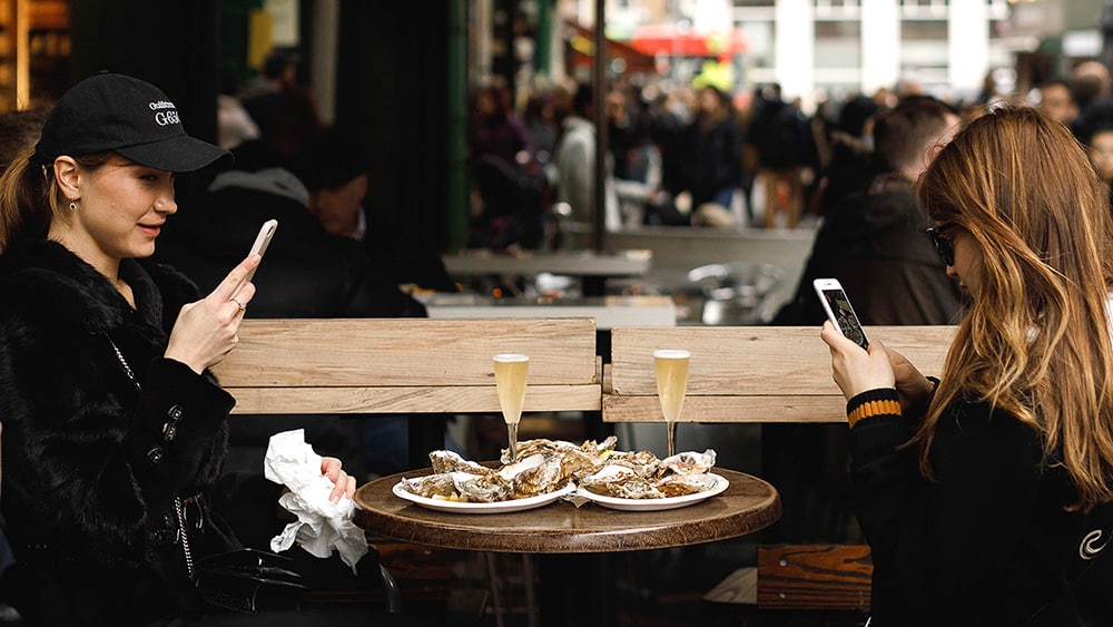 Two women taking photos of their oysters at a Borough market stall